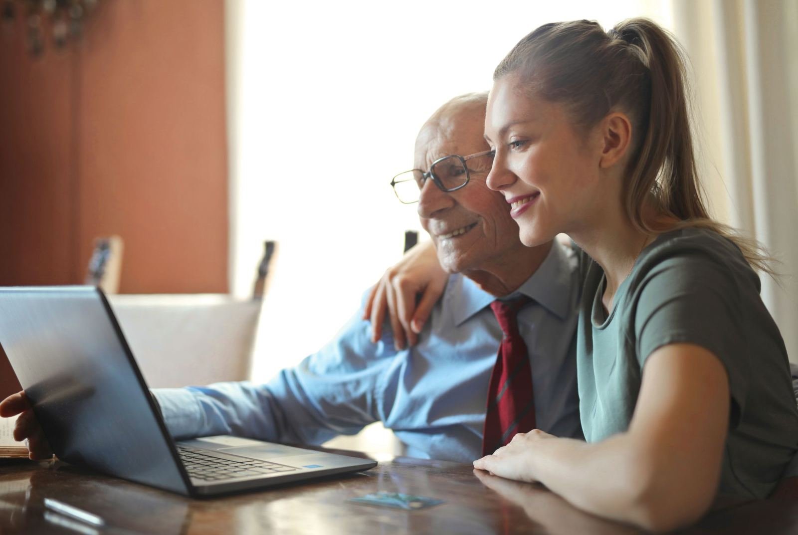 An elderly man and a young woman look at a computer screen and smile together
