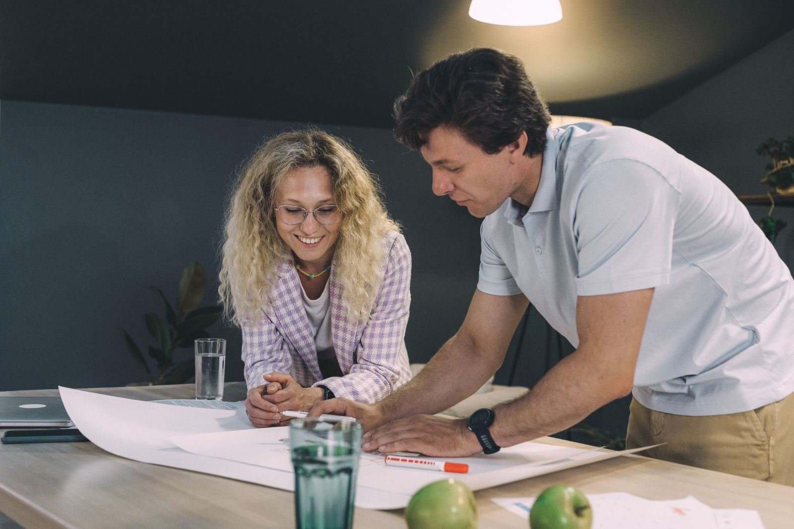 A man and woman review a large document together at a wooden table