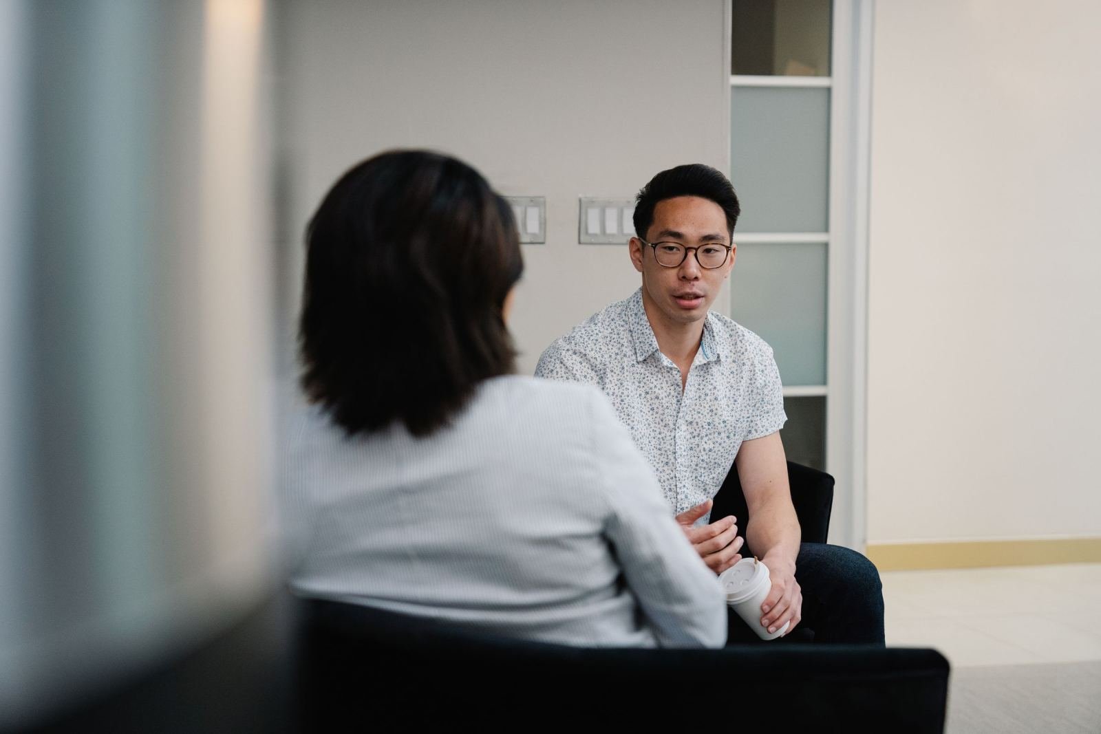 In a quiet office, a man wearing glasses speaks with a woman.