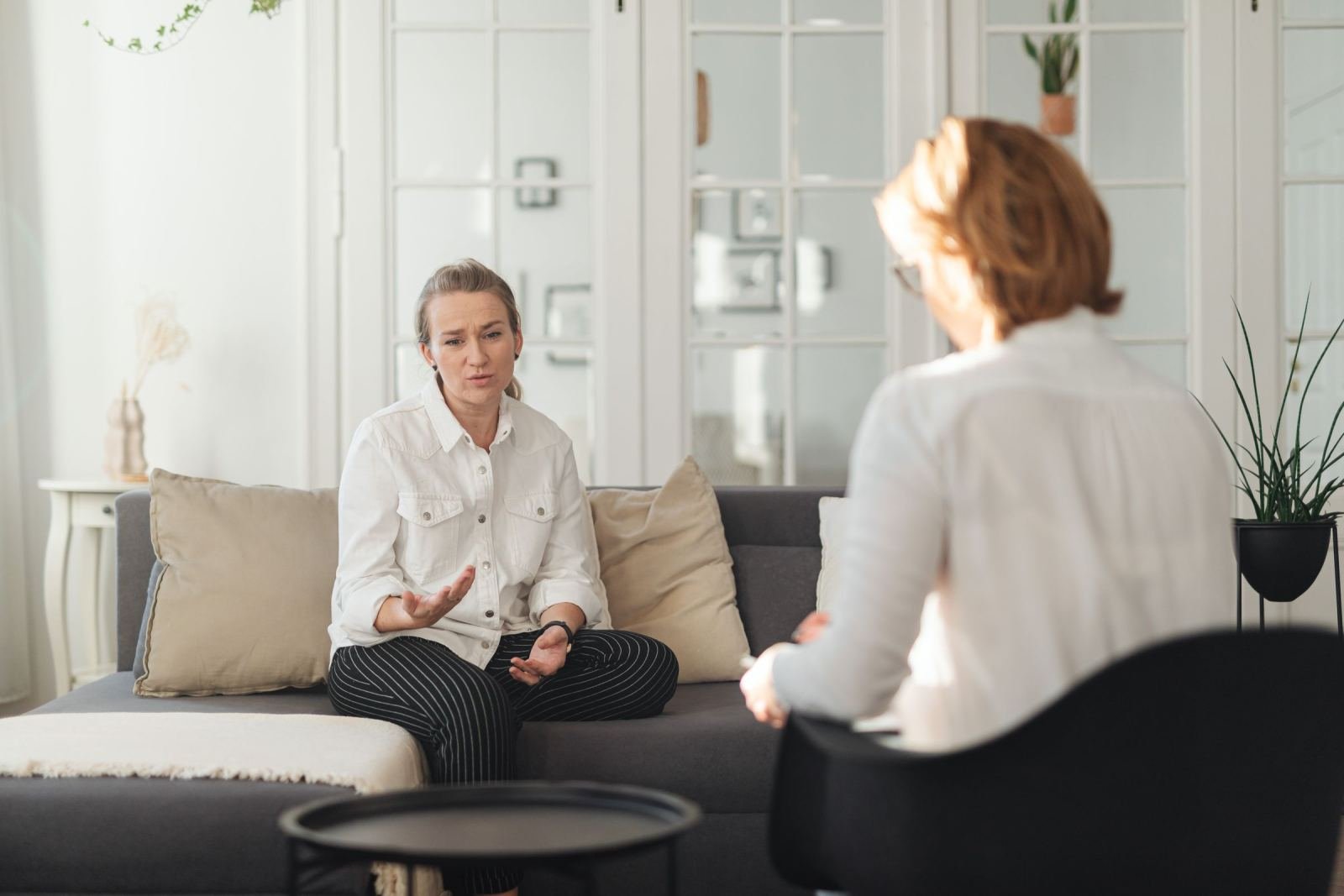 A woman gestures while speaking to a counselor in a bright, modern room