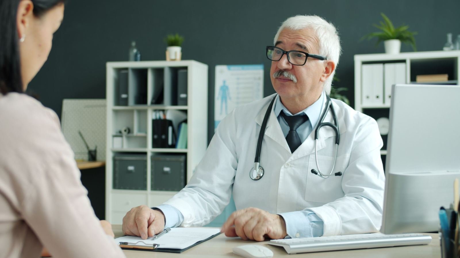 A doctor in a white coat talks with a patient in a bright office