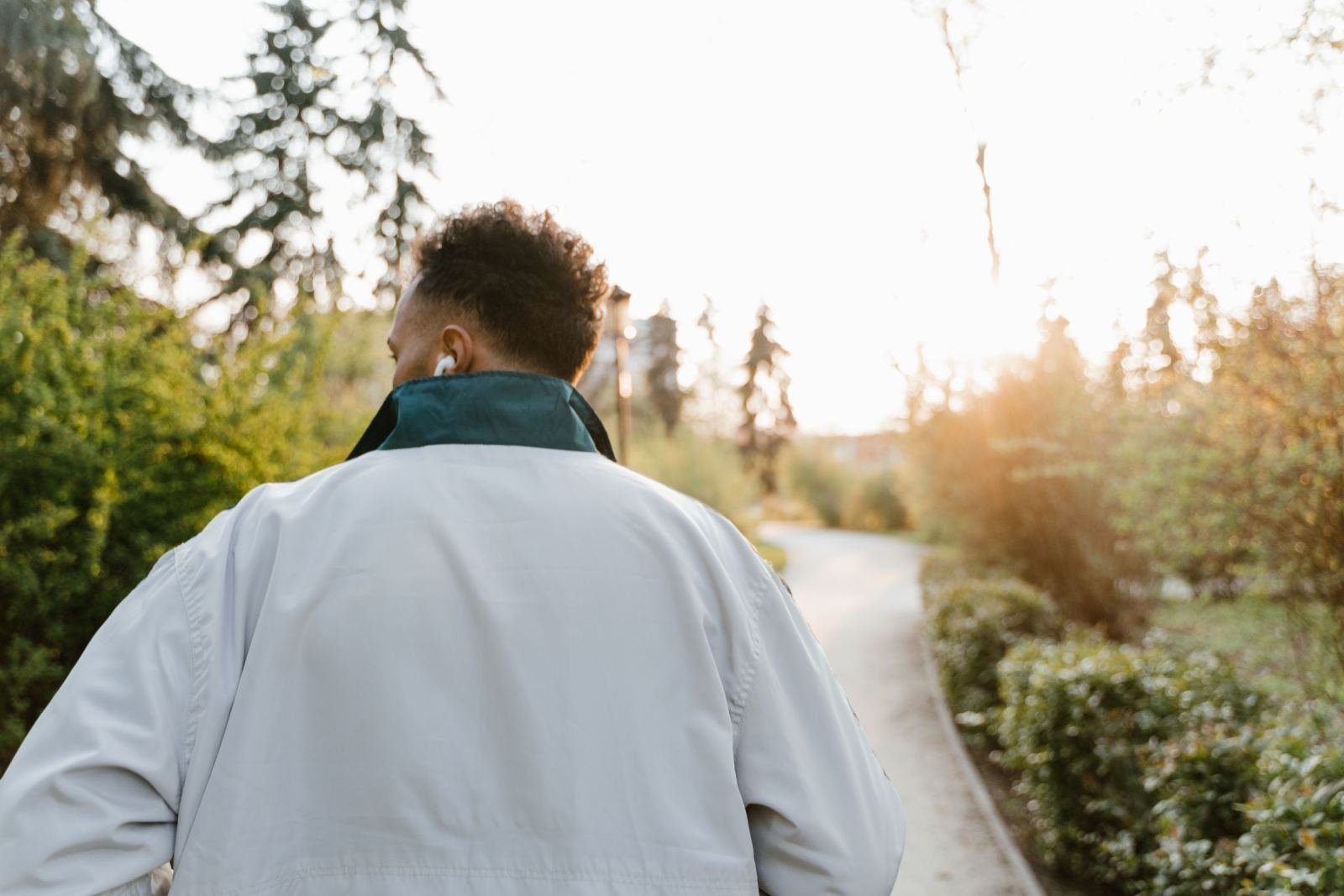 A man seen from behind walks along a paved path in a park