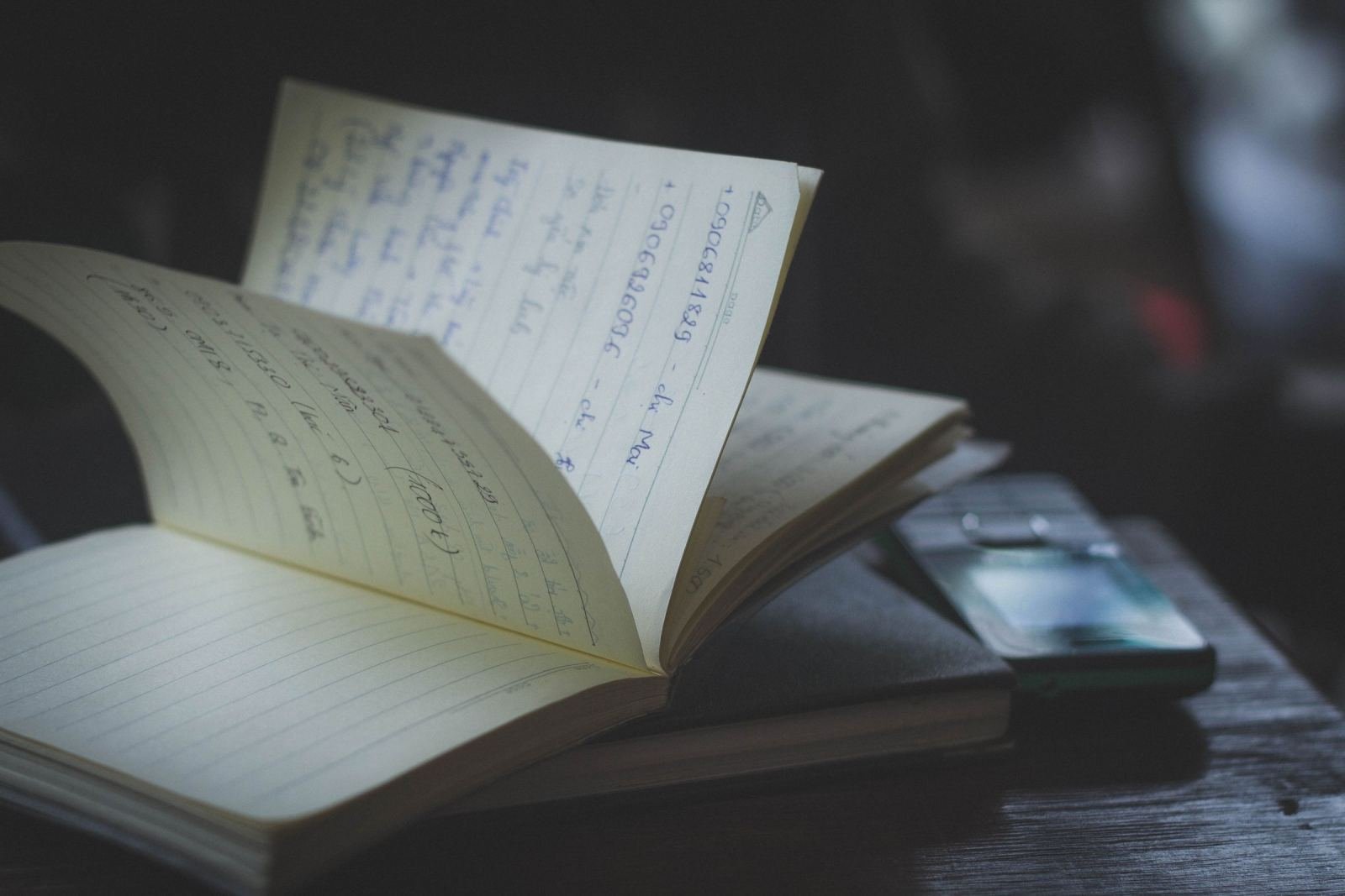 An open notebook with handwritten notes and a smartphone on a wooden table
