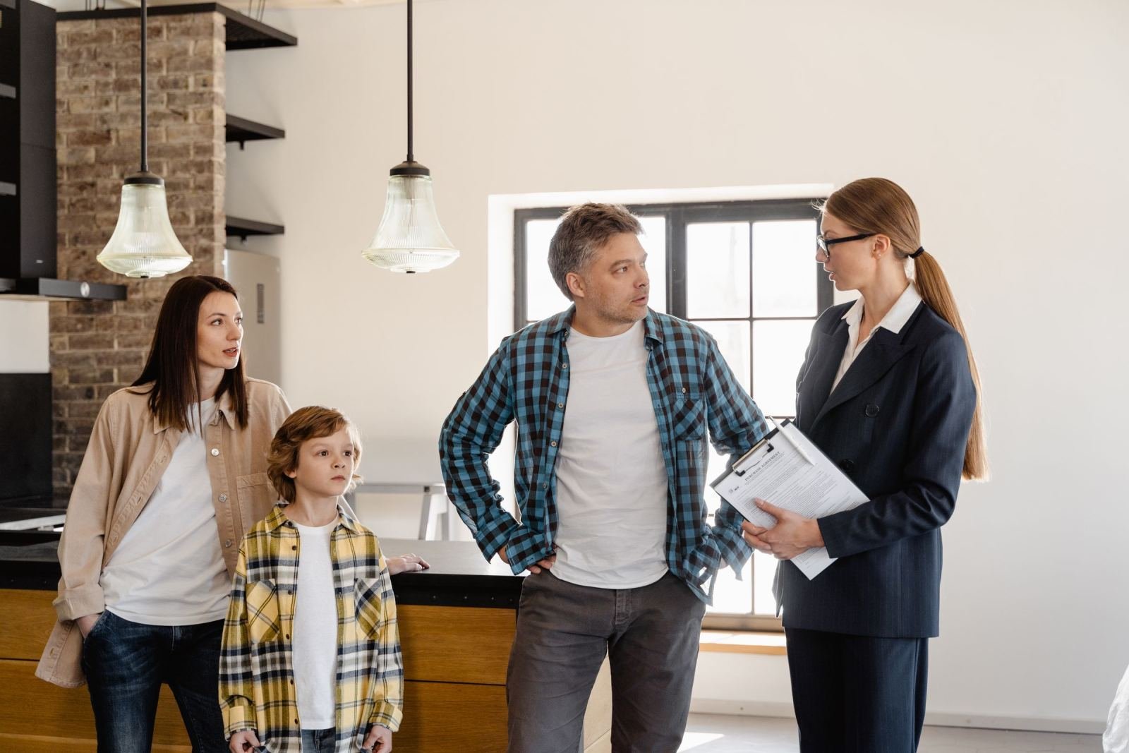 A professional woman holds a clipboard while talking to a man, woman, and child in a kitchen.