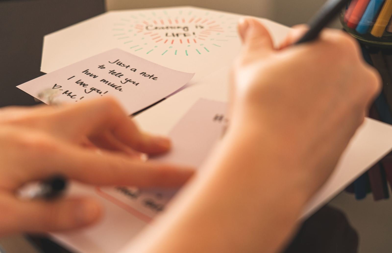 A person writing a note on a desk next to a card that says I love you