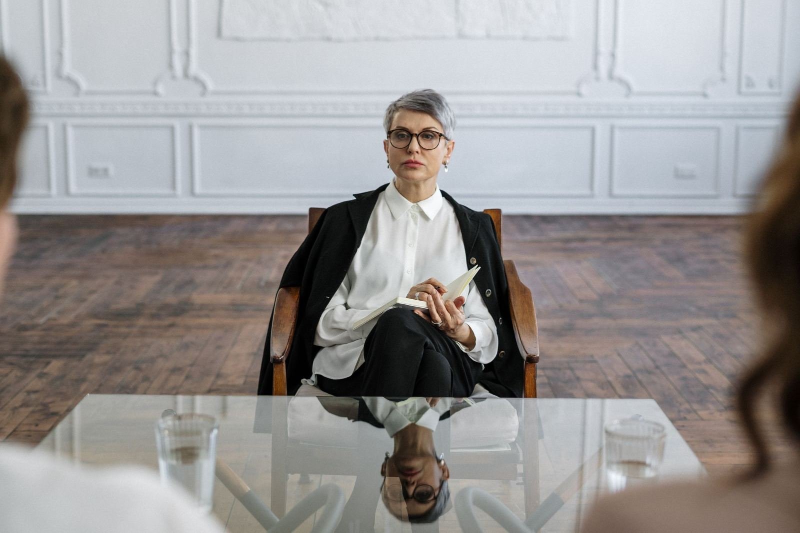 A woman with glasses and a notebook sits in a chair facing two people