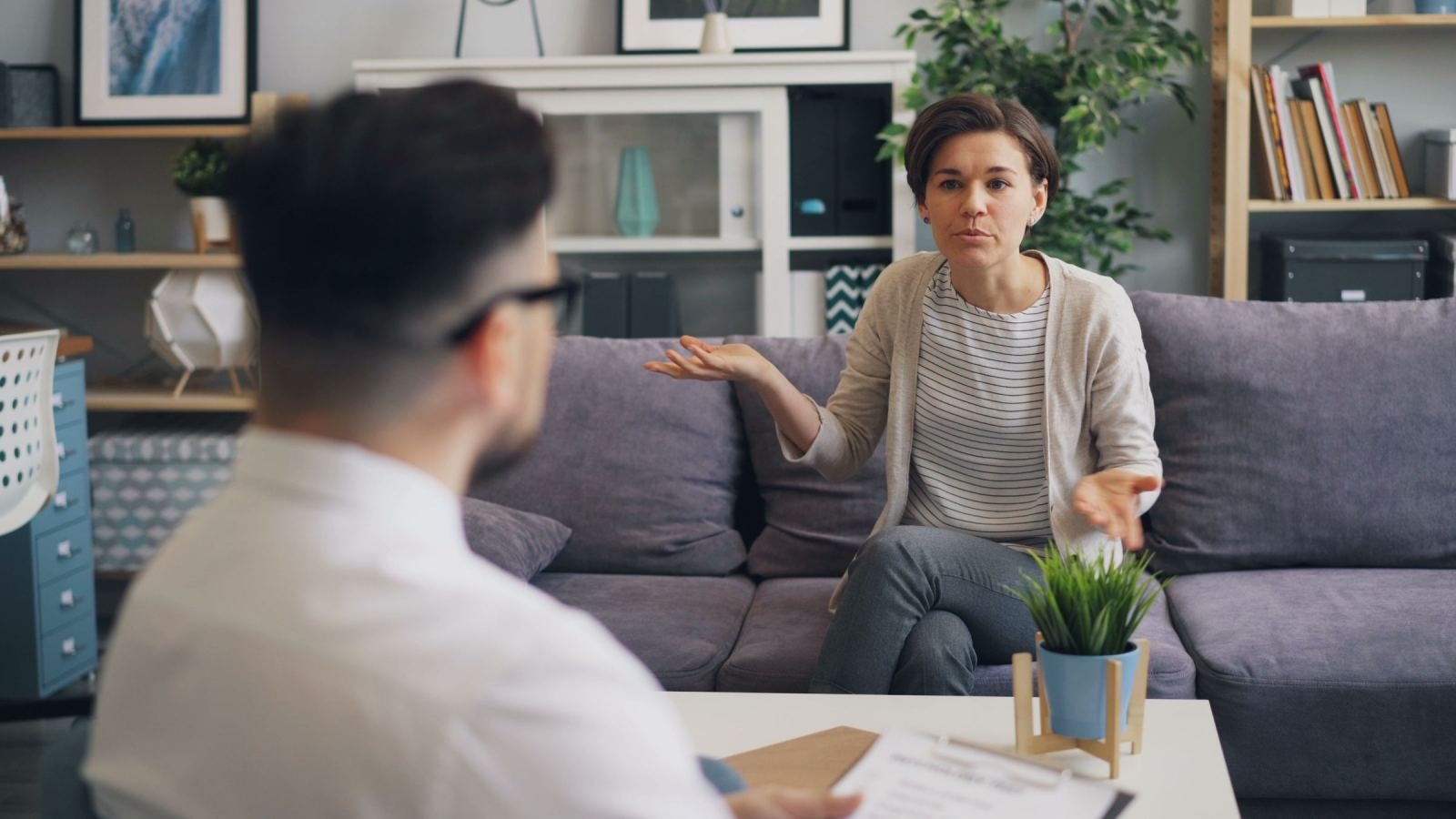 A woman makes a gesture as she speaks to a man in a bright office.