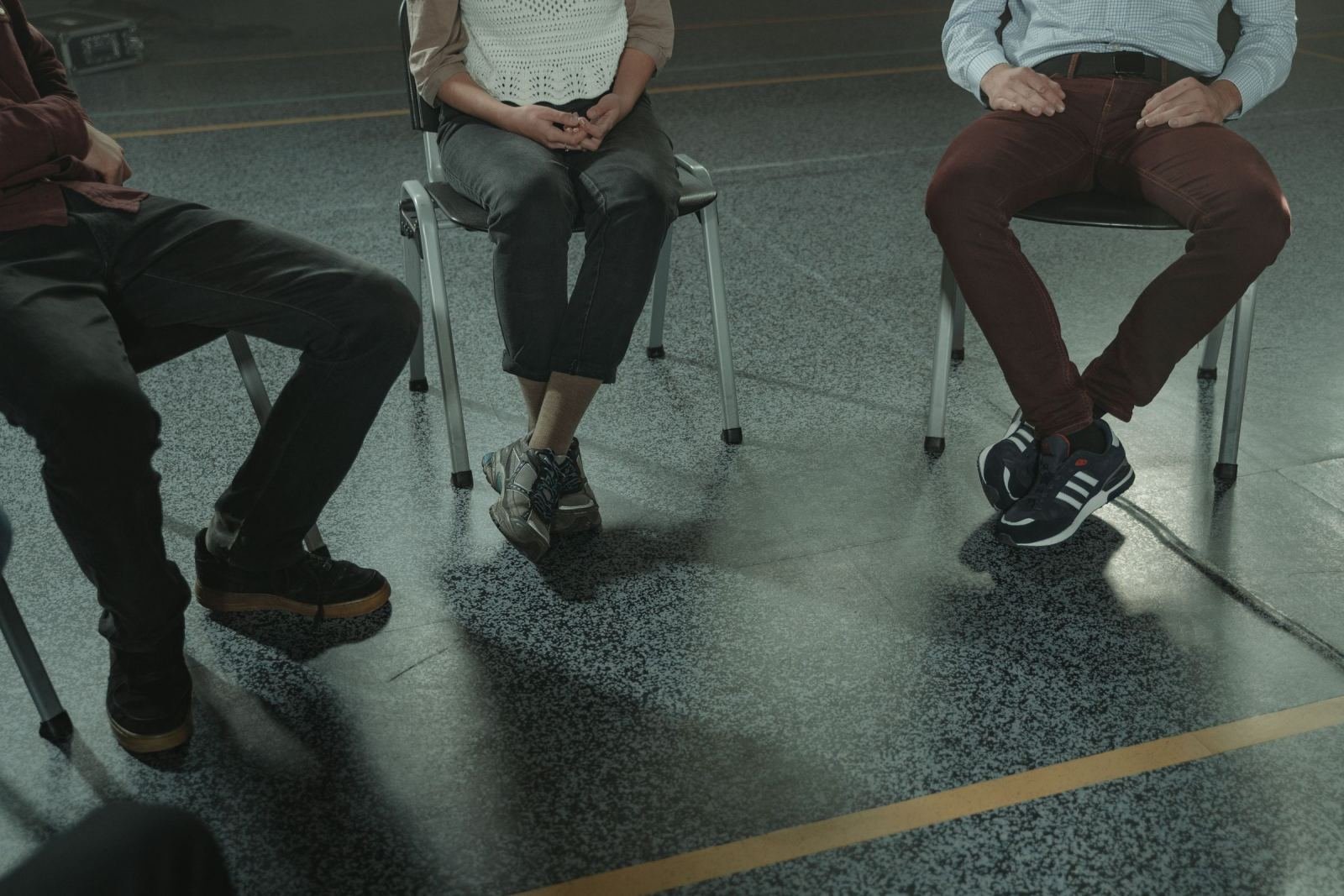 Three people sit in a circle of chairs in a big room.