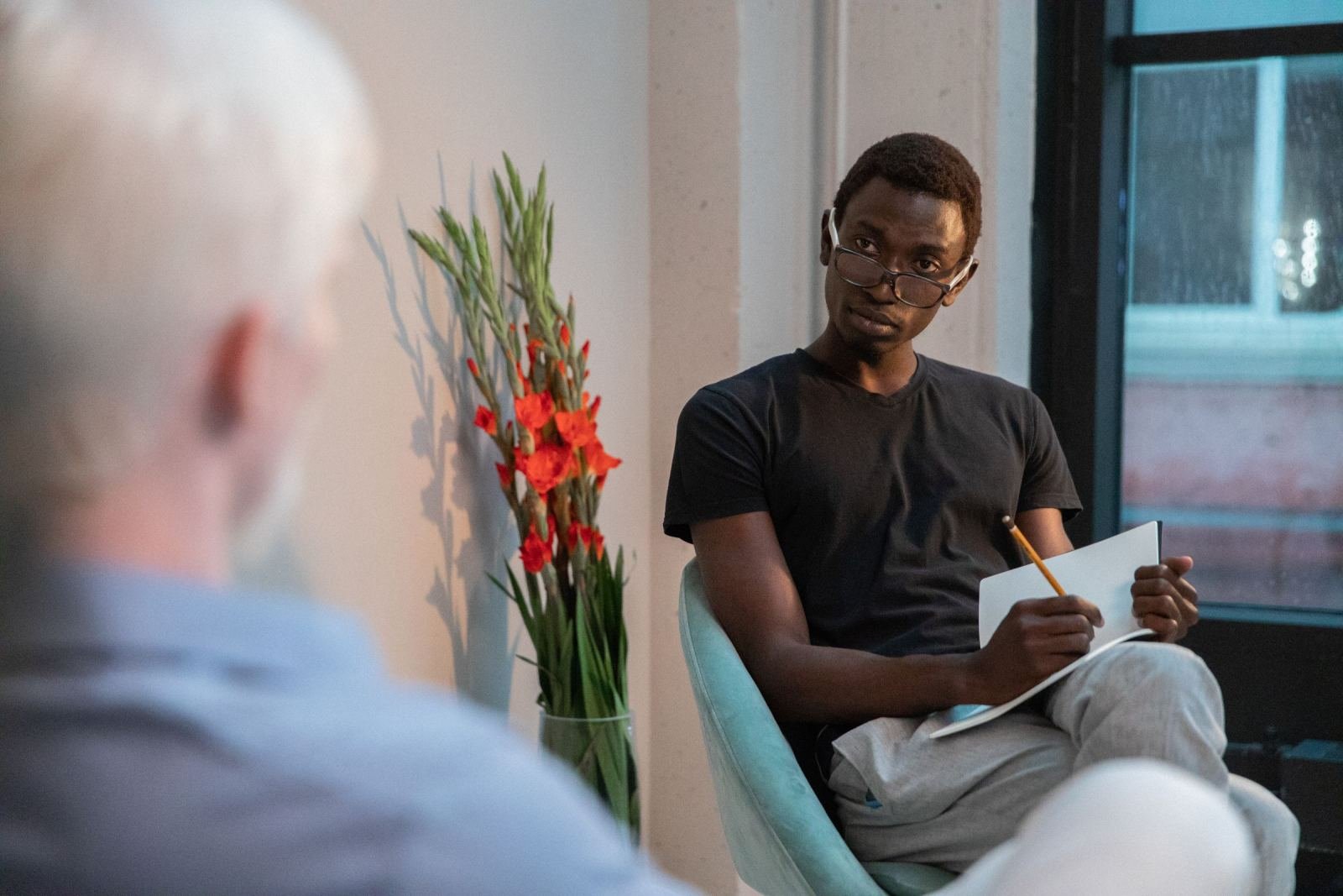 A man with glasses and a notebook listens to another person in an office