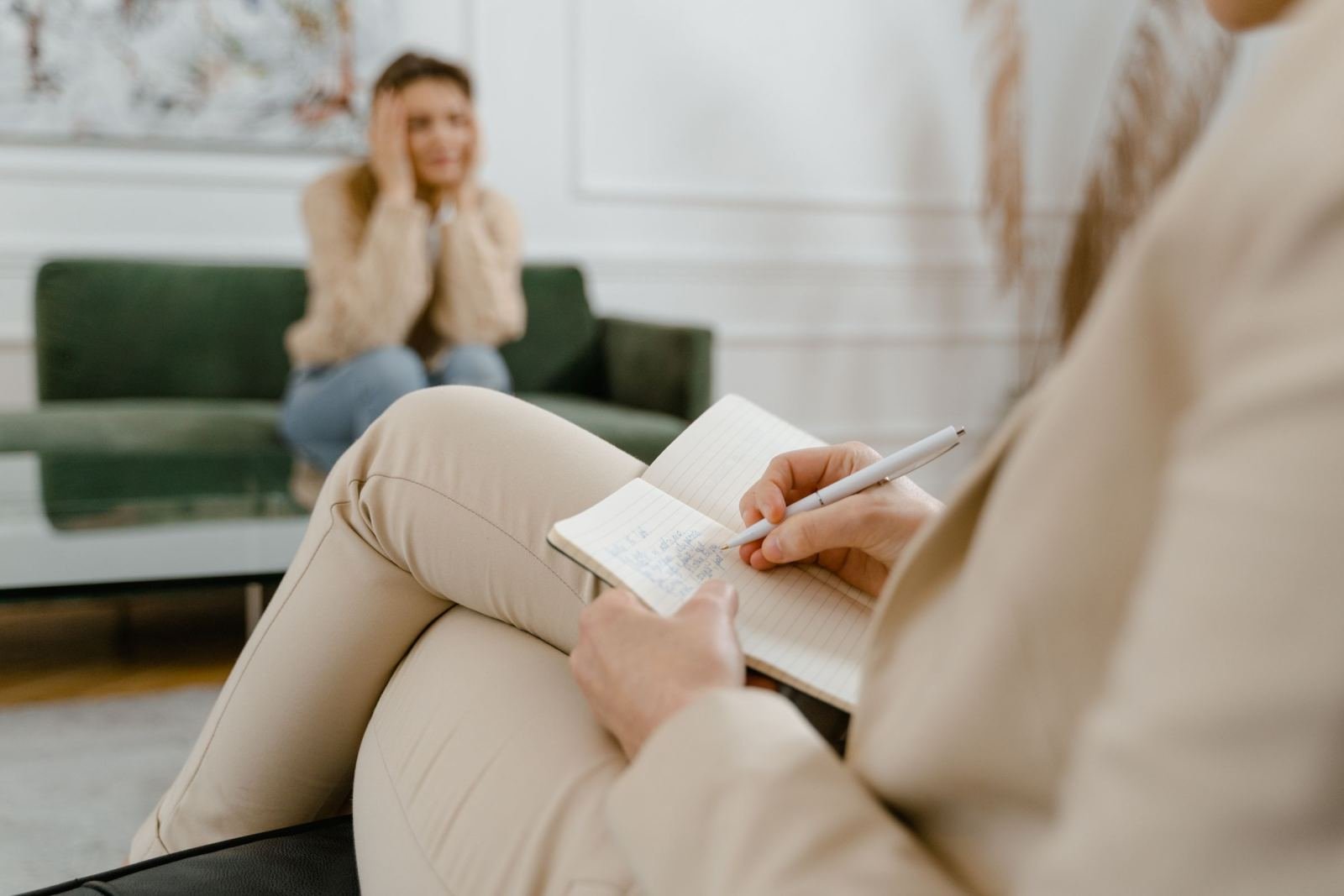 A counselor takes notes while a woman sits on a green sofa in the background