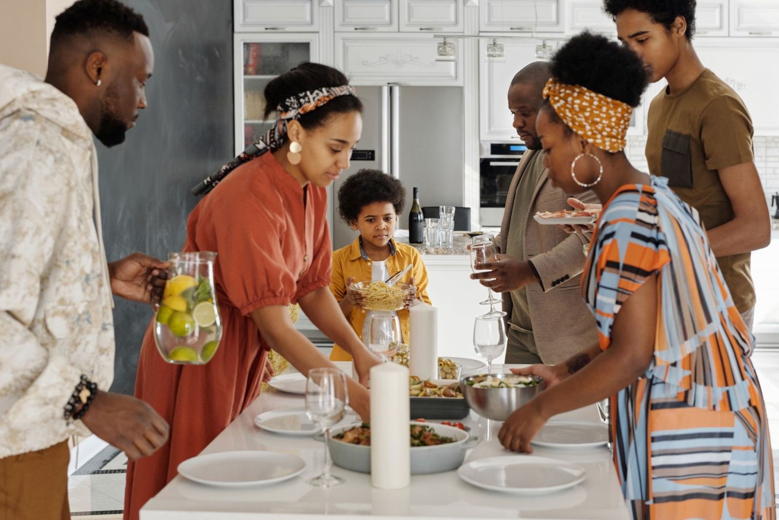 A family gathers around a white table to set out a meal together