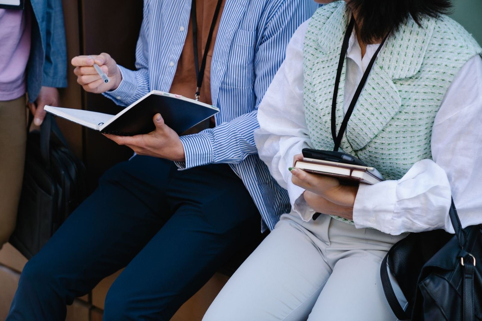 Two people sitting side by side holding notebooks and a pen
