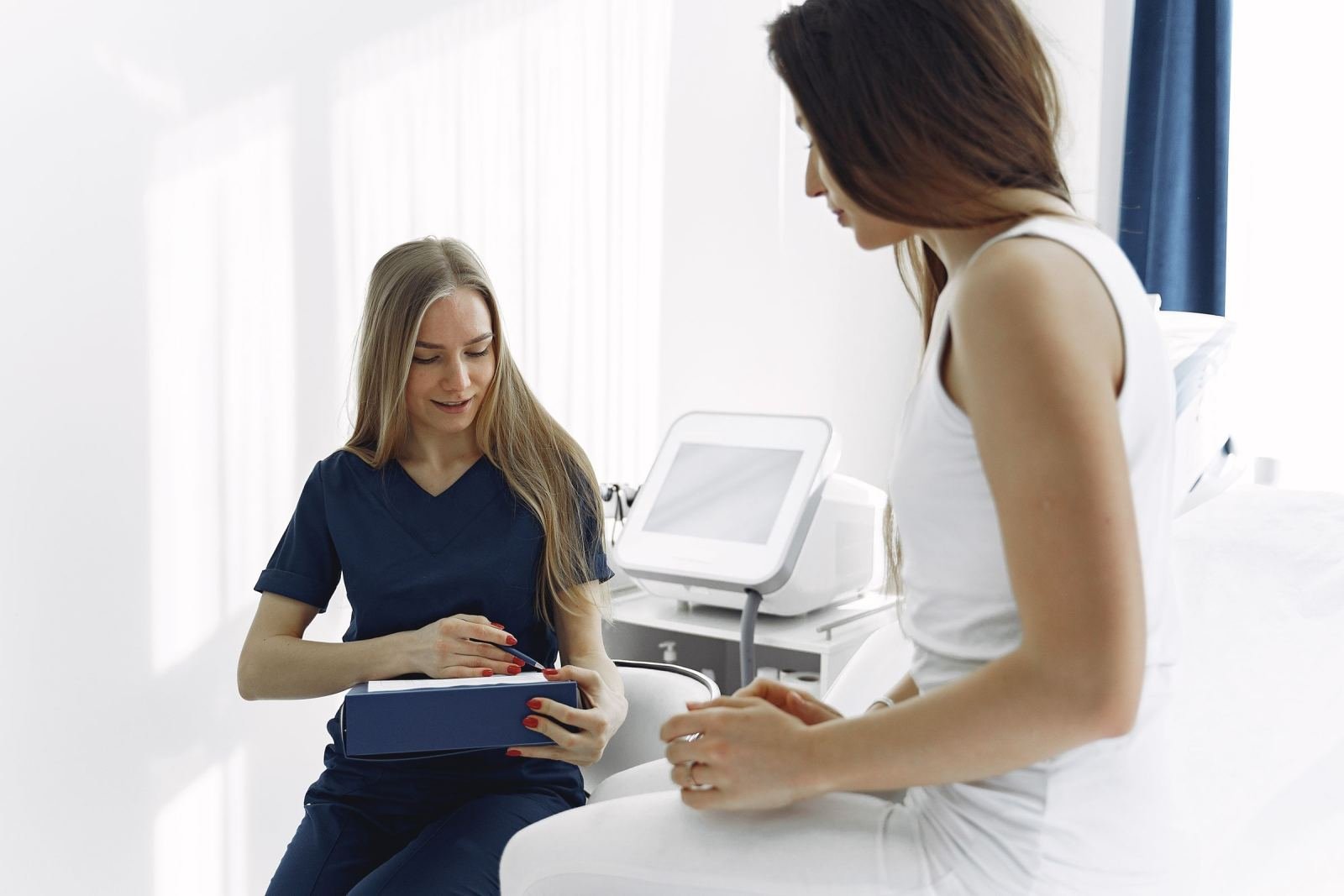 A clinician in scrubs talks with a patient sitting on an examination table