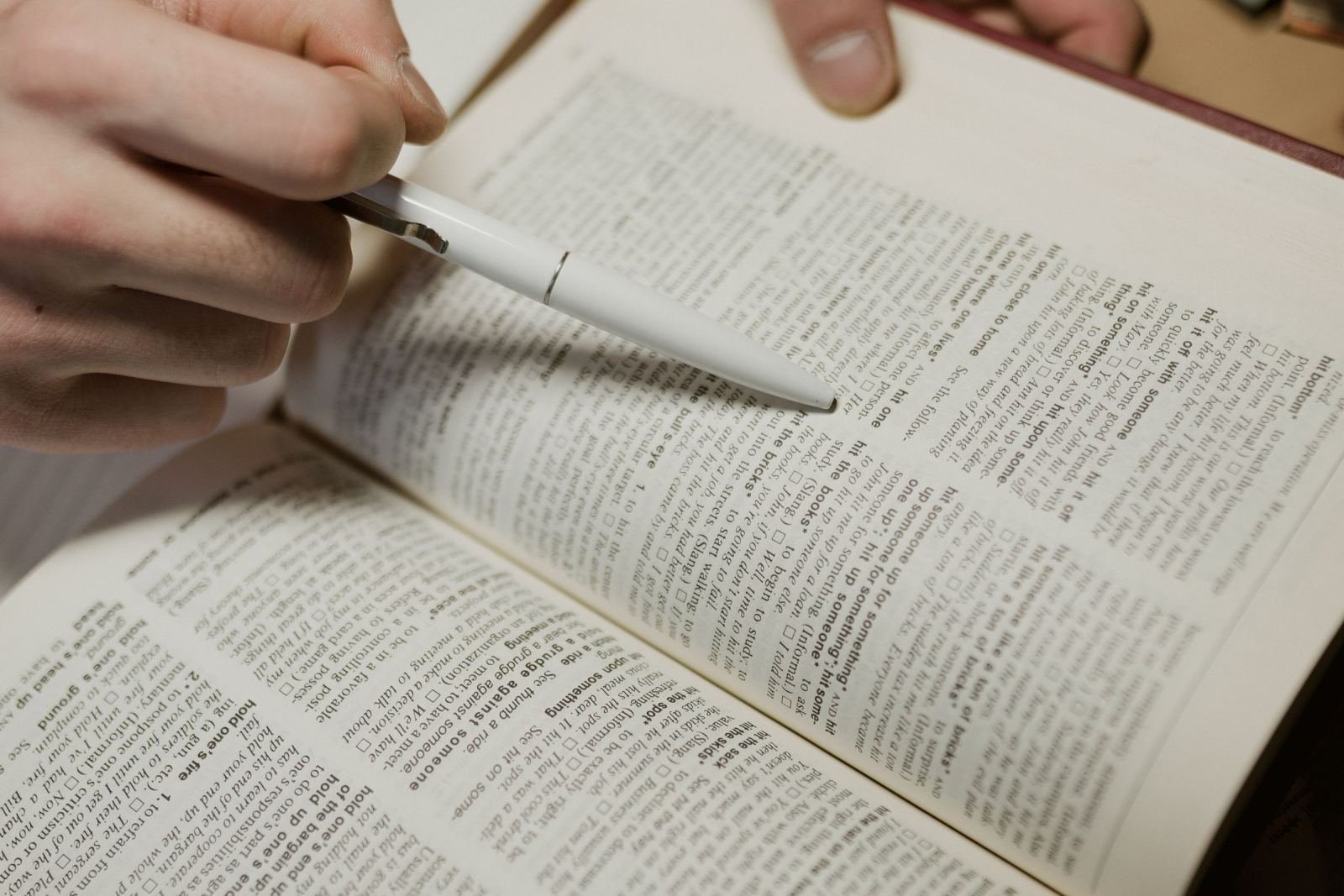 Hands using a white pen to point to text in an open book