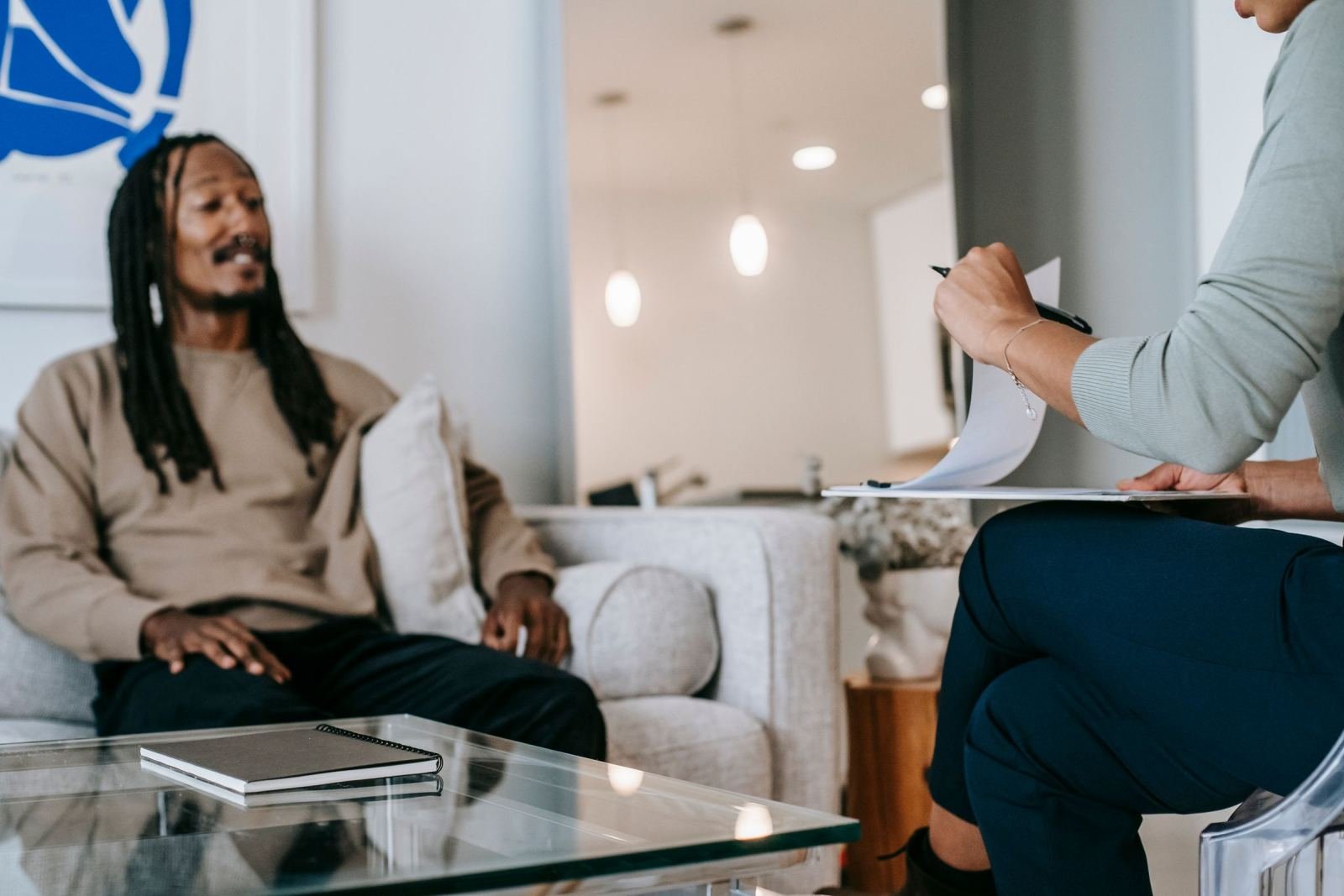 A man sits on a sofa talking to a counselor holding a clipboard