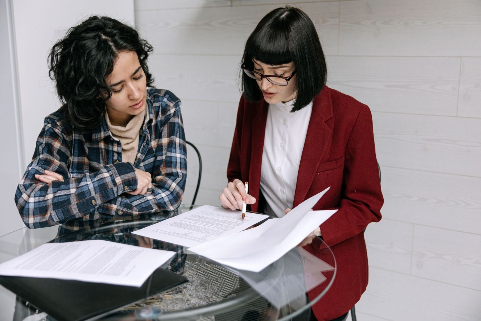 Two women review printed documents together at a glass table