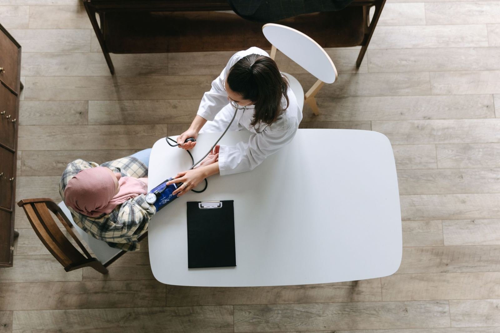 A clinician in a white coat checks a patient's blood pressure at a white table