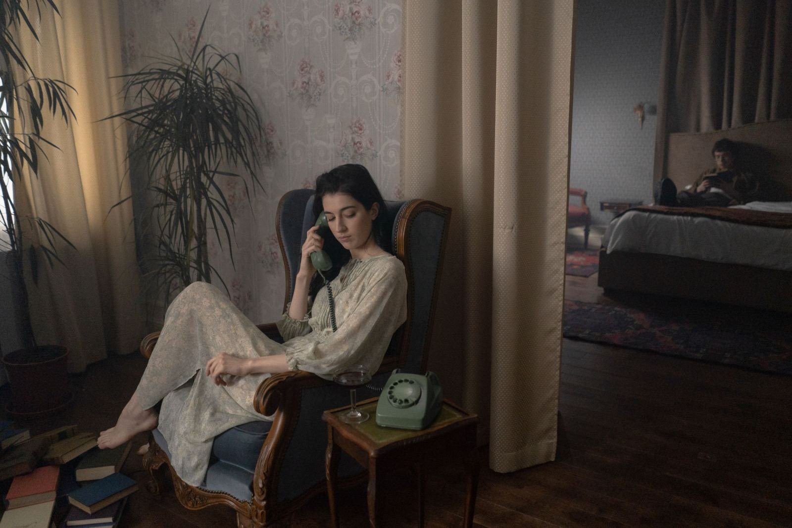 A woman in a dress talks on a vintage green telephone in a quiet room