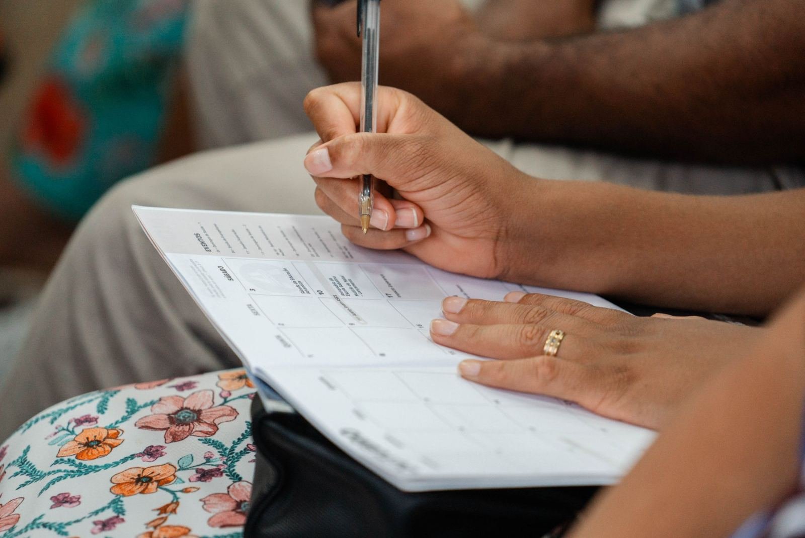A person using a pen to mark a date on a paper calendar