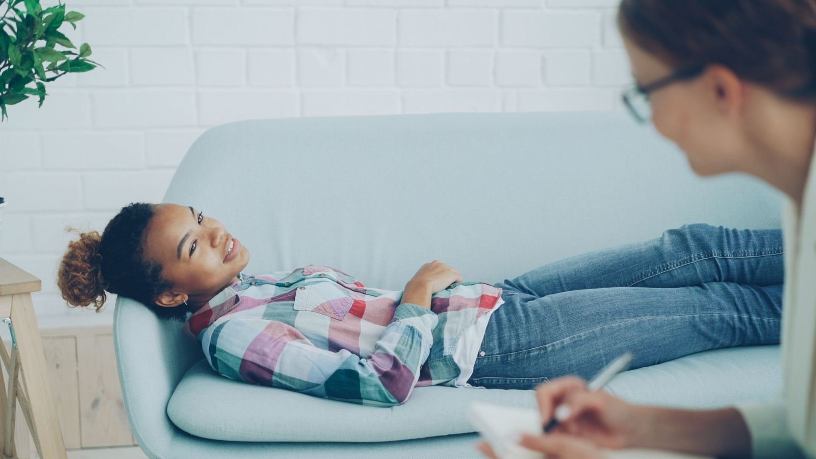 A therapist writes notes while a woman rests on a blue couch