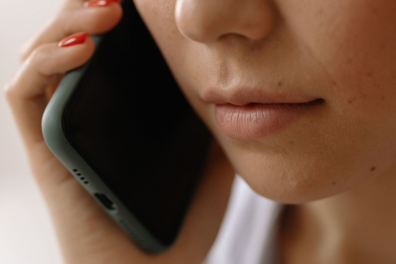 Close-up of a person with red nail polish holding a green smartphone to their ear