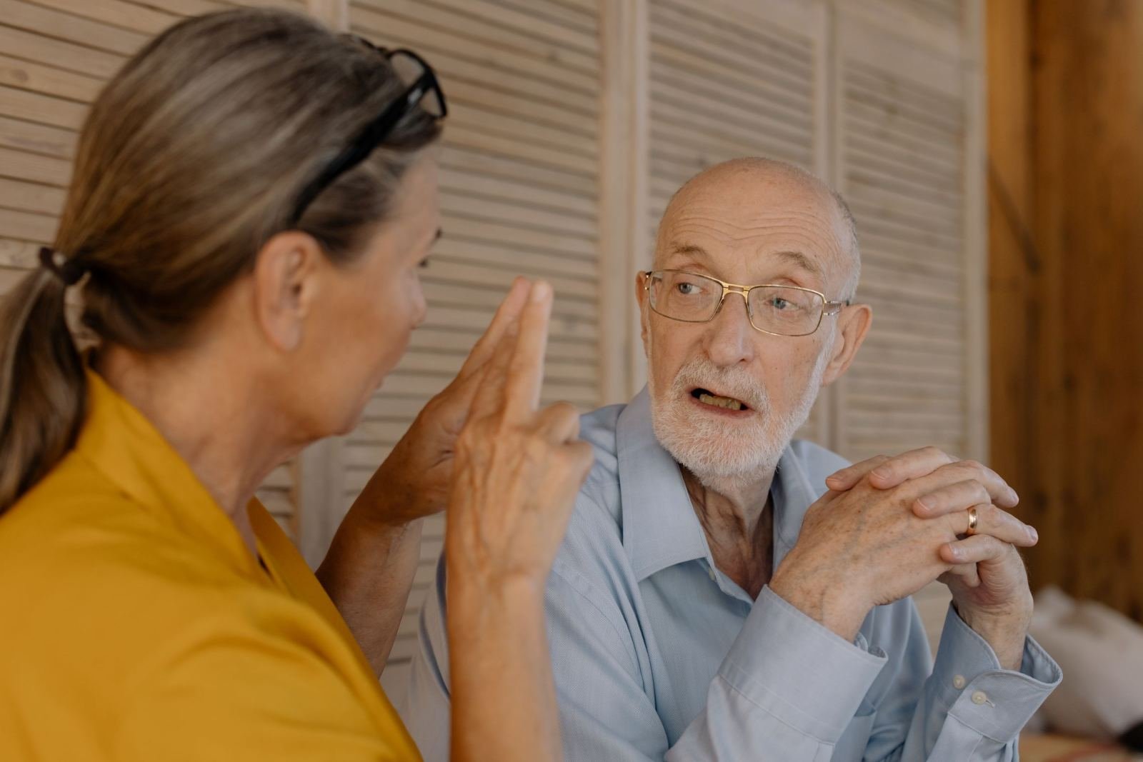 An older man listens to a woman who is gesturing with her hand while speaking
