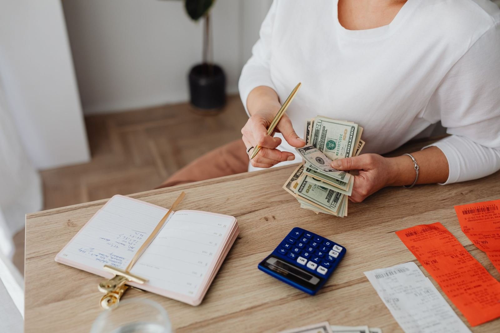 A person holding cash at a table with a calculator, notebook, and receipts