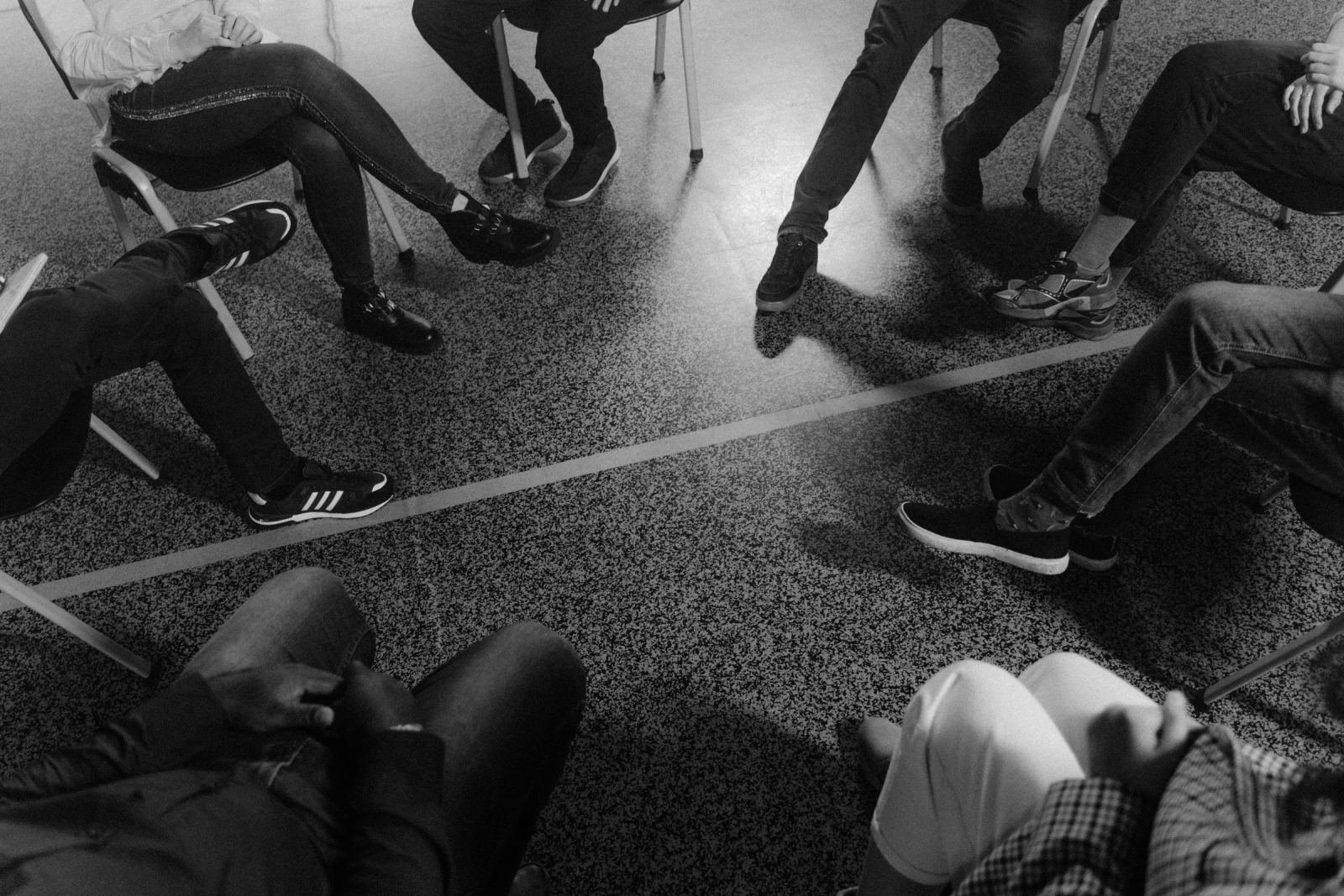 A group of people sitting in a circle of chairs in a black and white photo