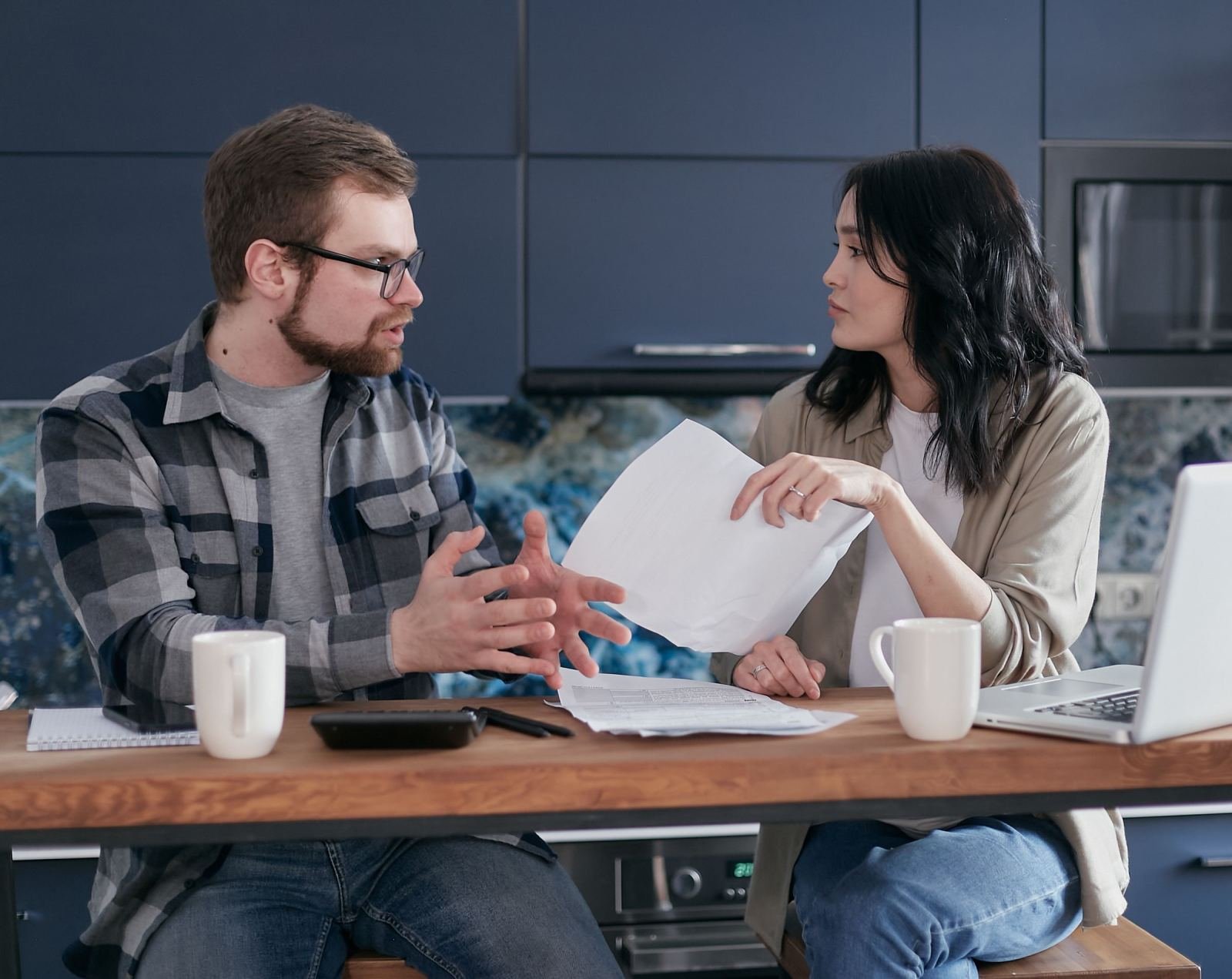 A man and woman sit at a kitchen table discussing papers