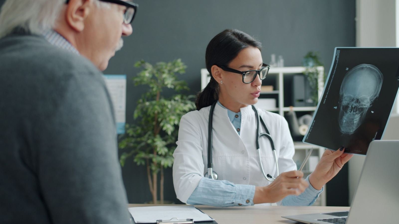 A doctor in a white coat shows an X-ray of a skull to an older patient