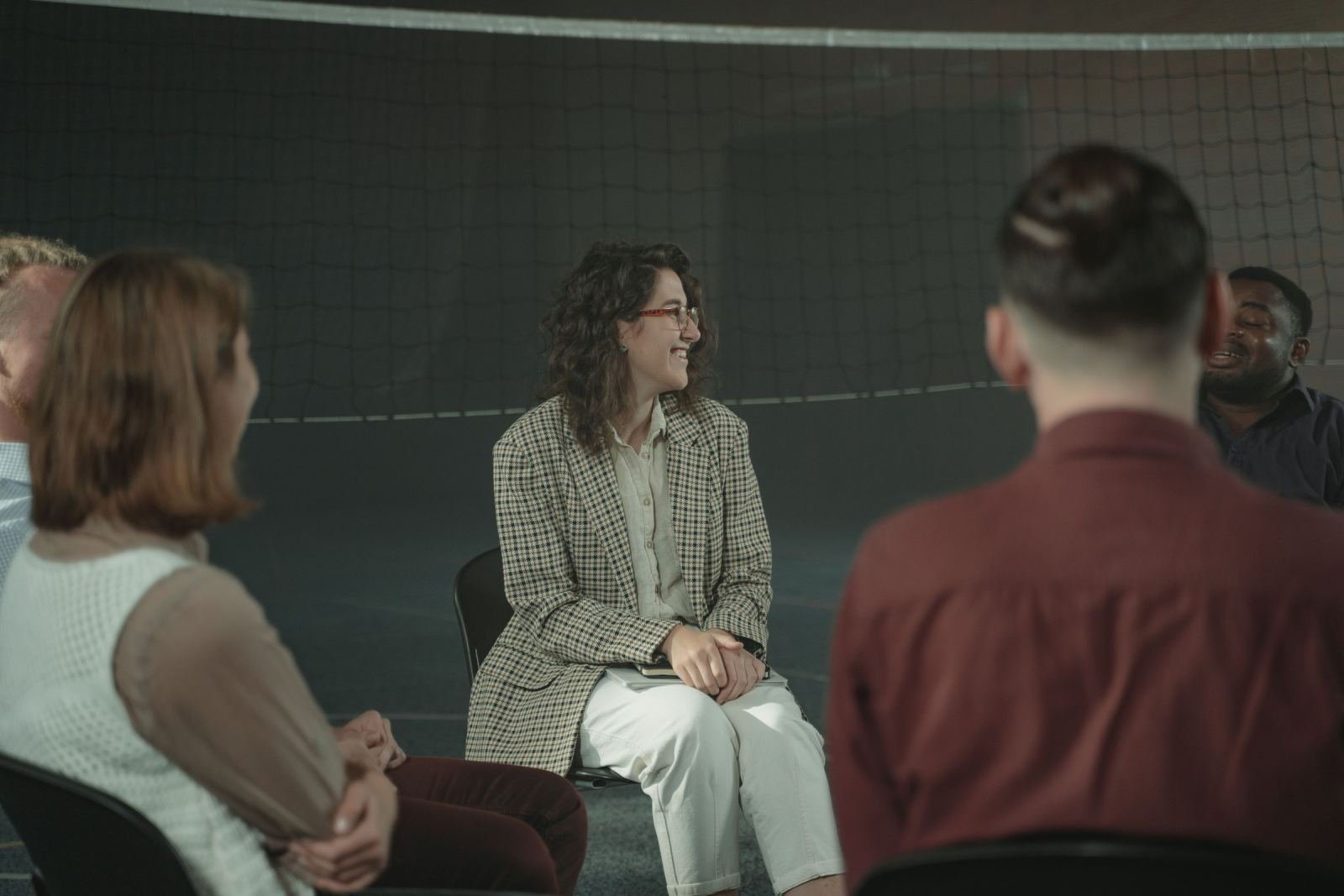 Adults sit in a circle talking in a dimly lit room