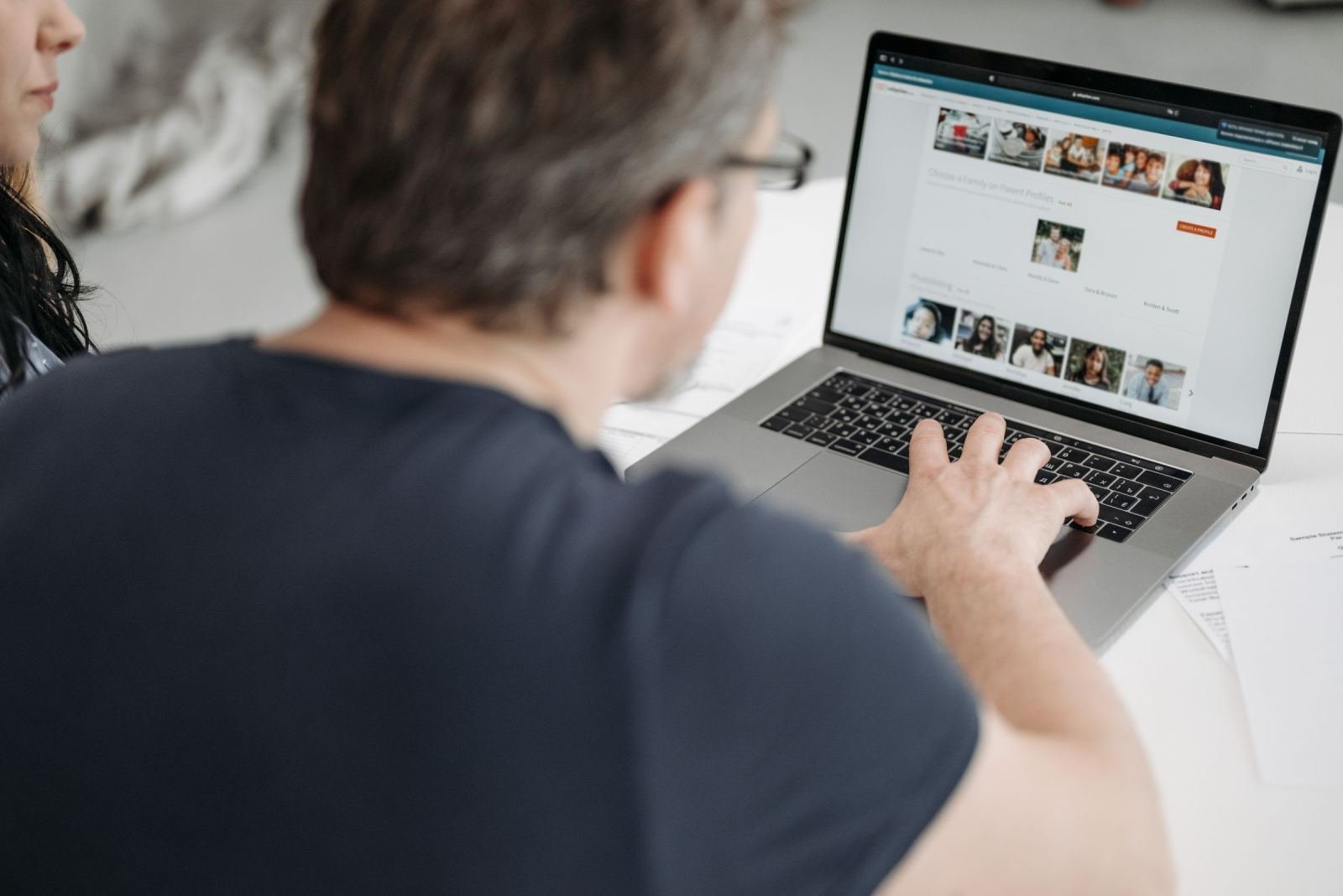 A man uses a laptop to browse a website with profile photos of people