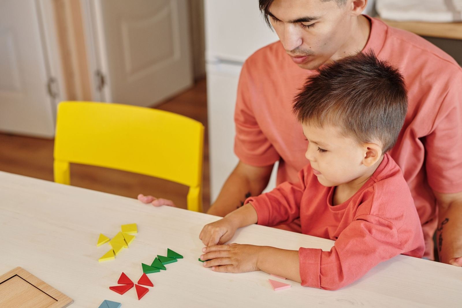 A man and a young boy arrange colorful geometric shapes on a white table