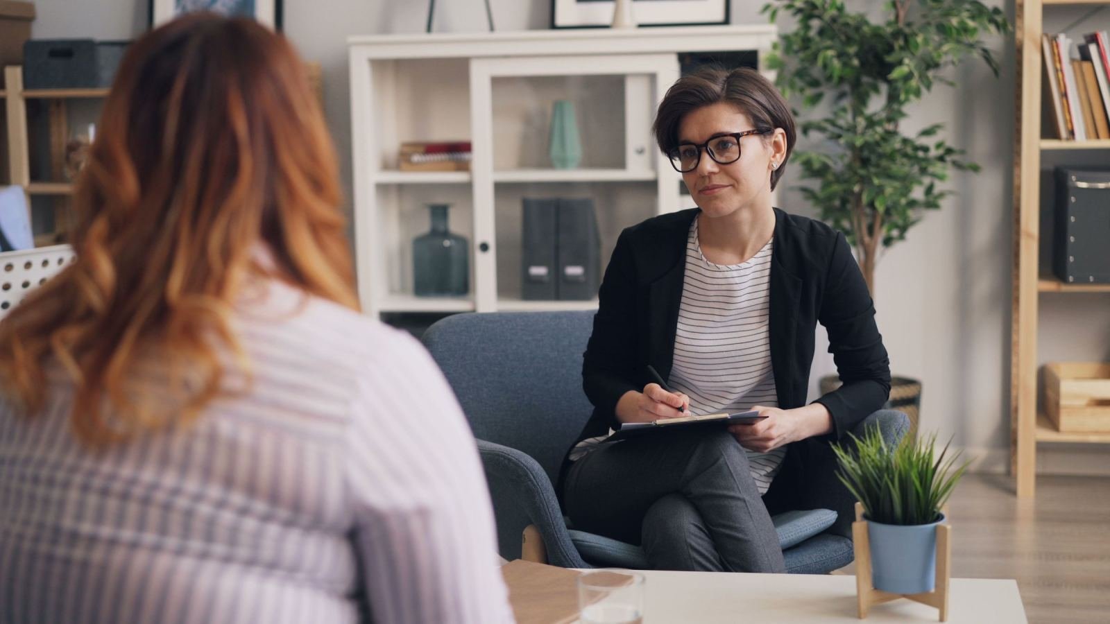 A counselor with a clipboard listens to a client in a bright office