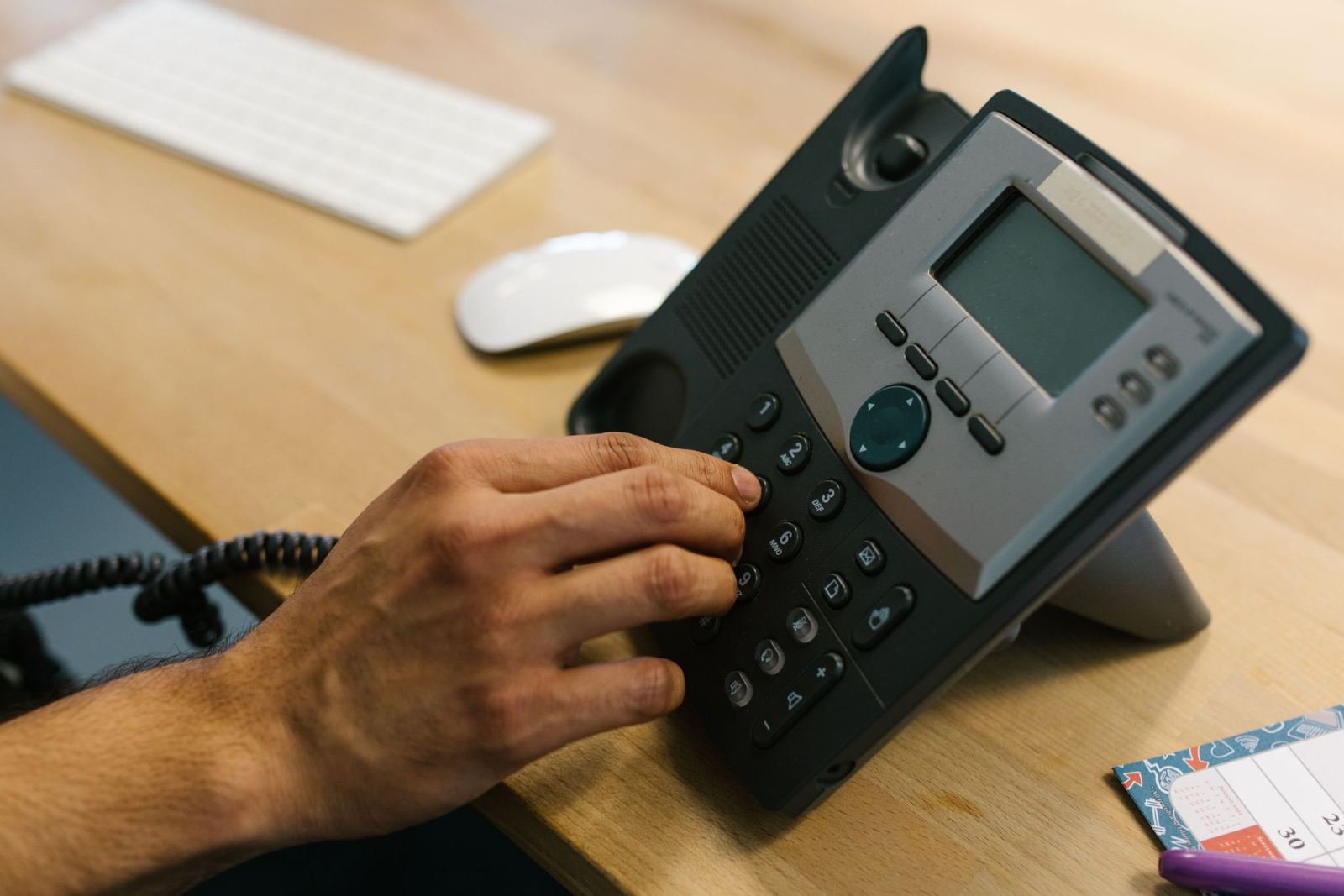 A person's hand dialing a number on a black desk phone