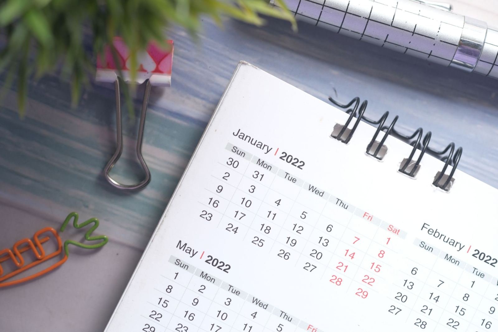 A spiral-bound calendar open to January and May 2022 sits on a blue desk