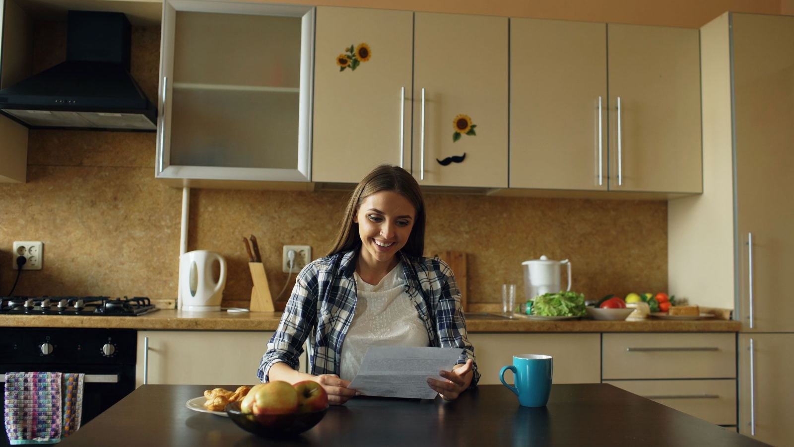 A woman smiling while reading a document at her kitchen table