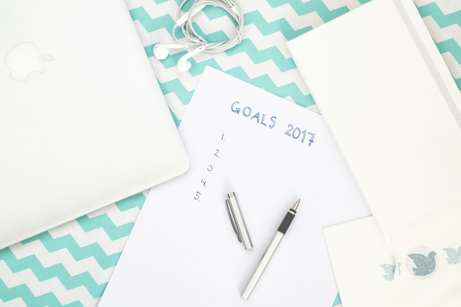 A laptop, earbuds, and a list titled GOALS 2017 on a teal chevron background