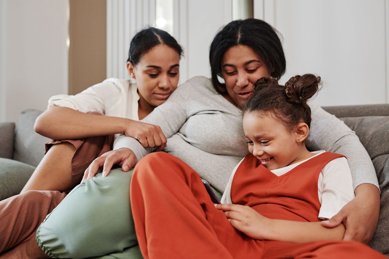 Three family members sit close together and smile on a gray couch