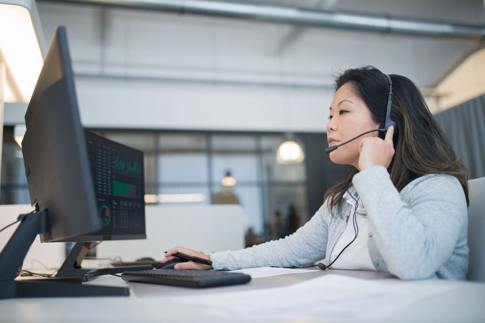 A woman with a headset on sits at a desk in an office.