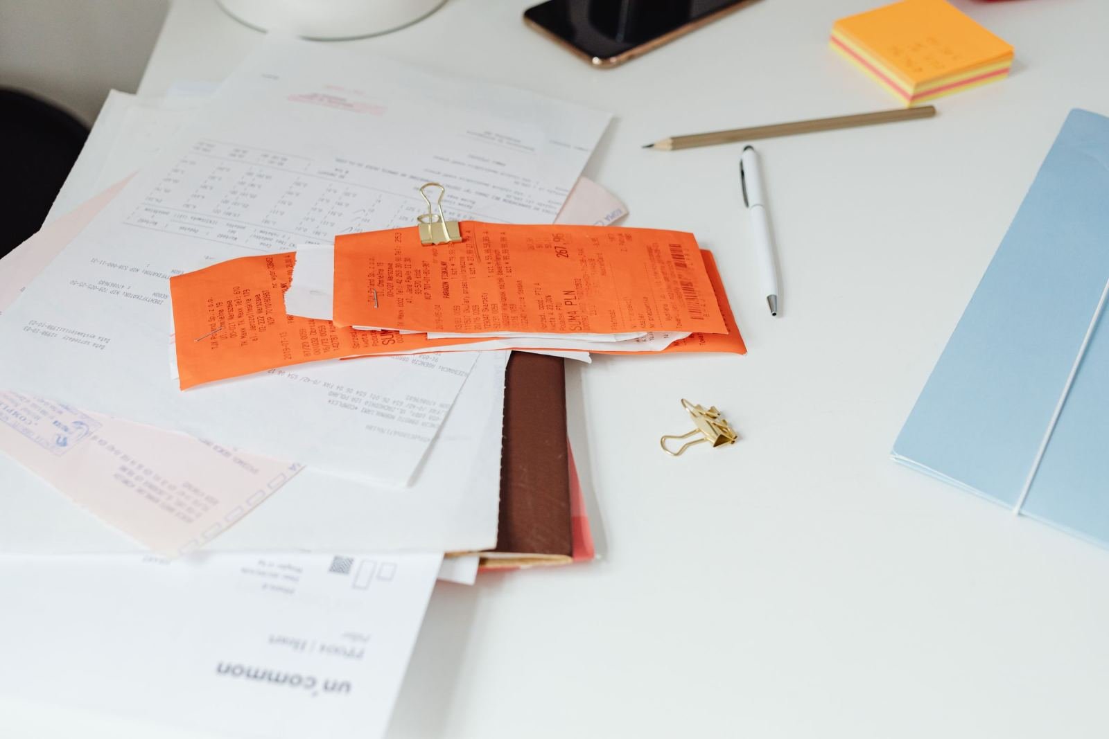 A pile of papers and orange receipts with a binder clip on a white desk