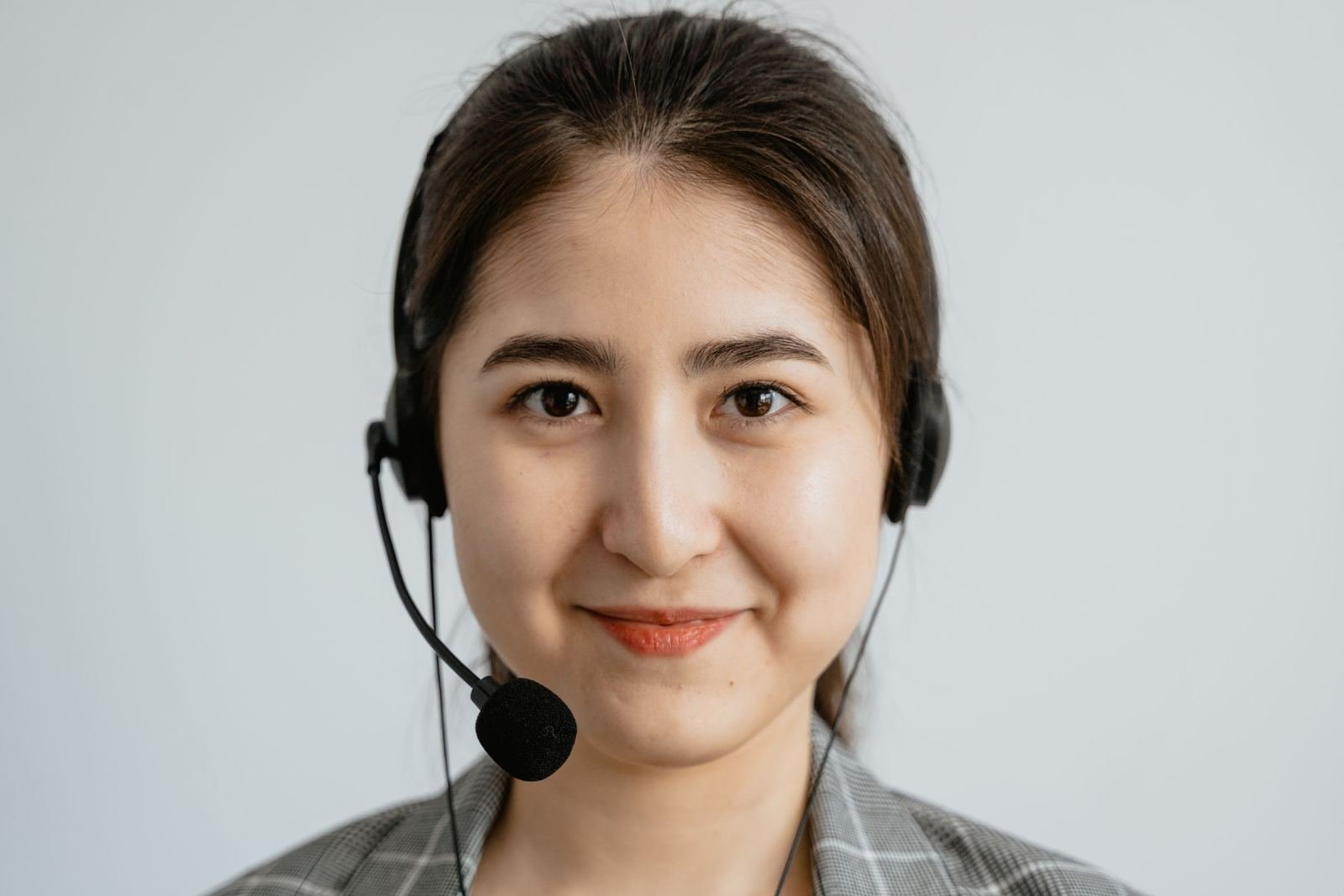 A woman wearing a headset and a plaid blazer smiles at the camera