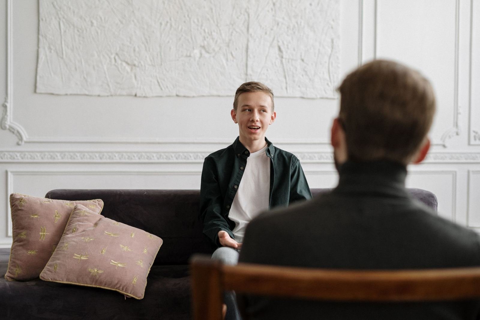 A gray sofa holds a young man as he talks with his counselor.
