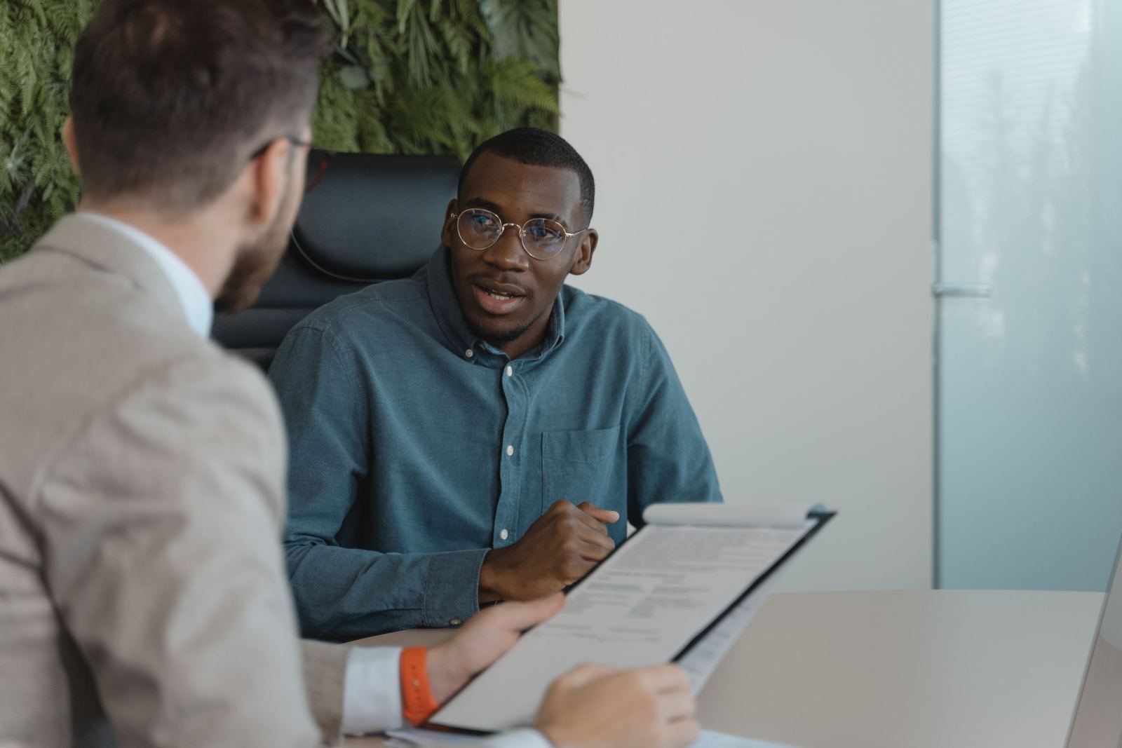 A man in glasses speaks with another person who is holding a clipboard