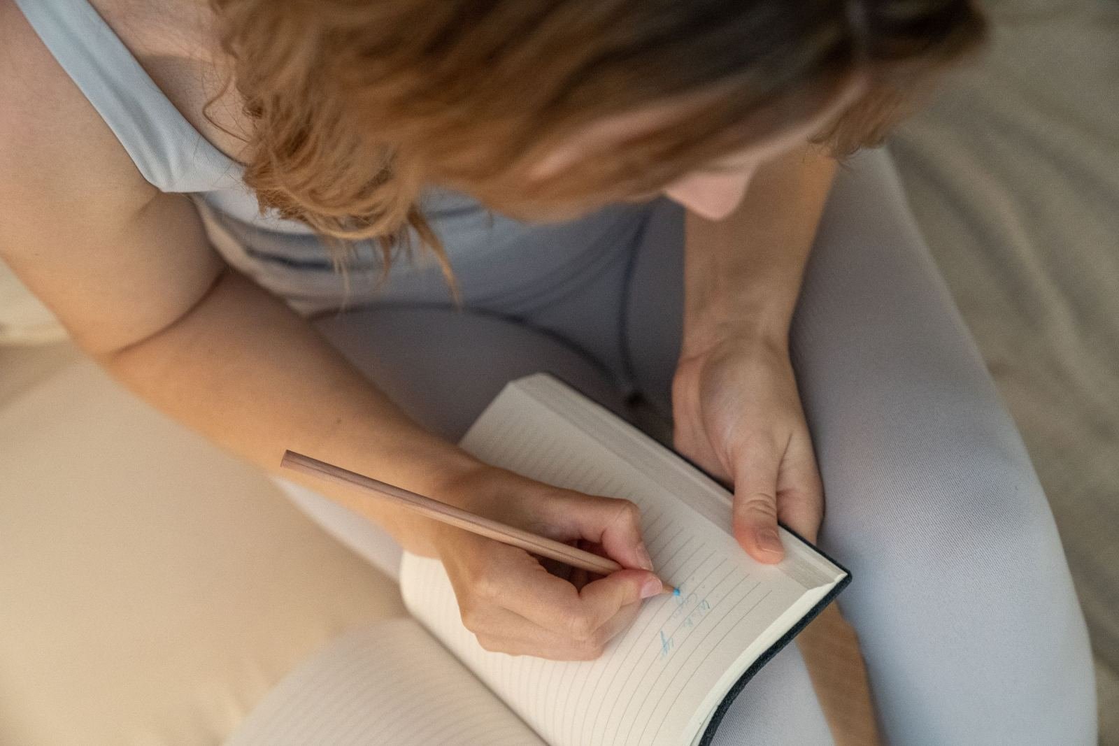 Someone writes in a ruled notebook using a pencil.