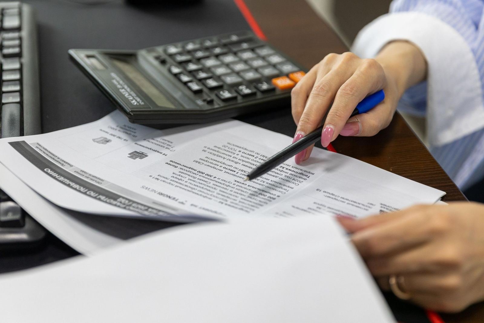 A person uses a pen to point to details on a printed document next to a calculator