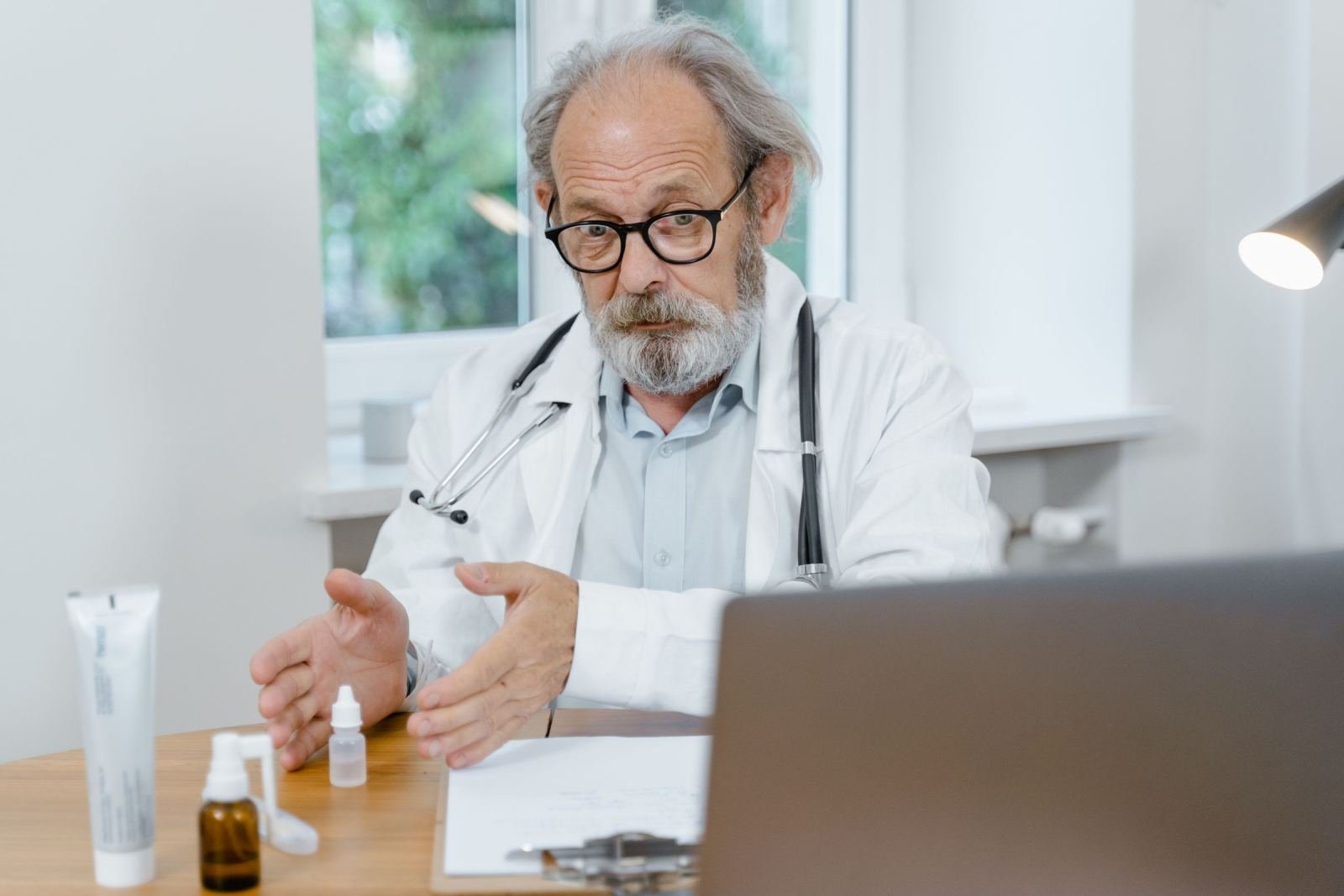A doctor in a white coat gestures while looking at a laptop screen