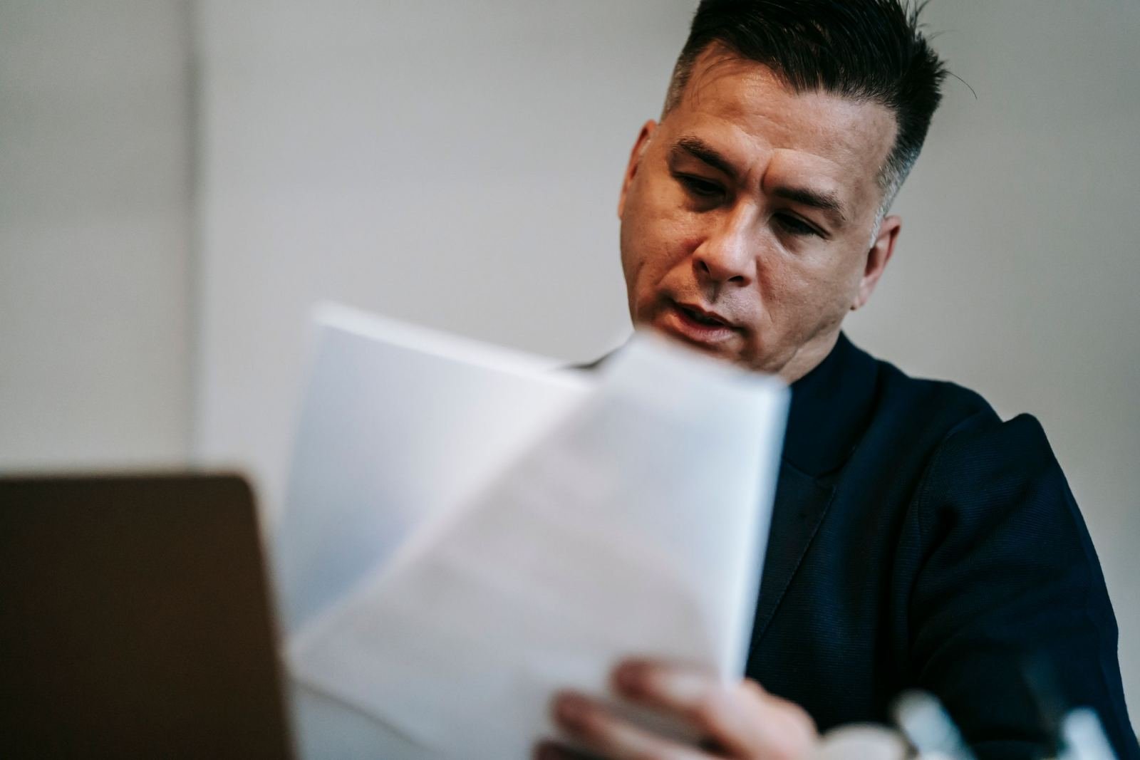 A man reads a document while sitting in front of a laptop