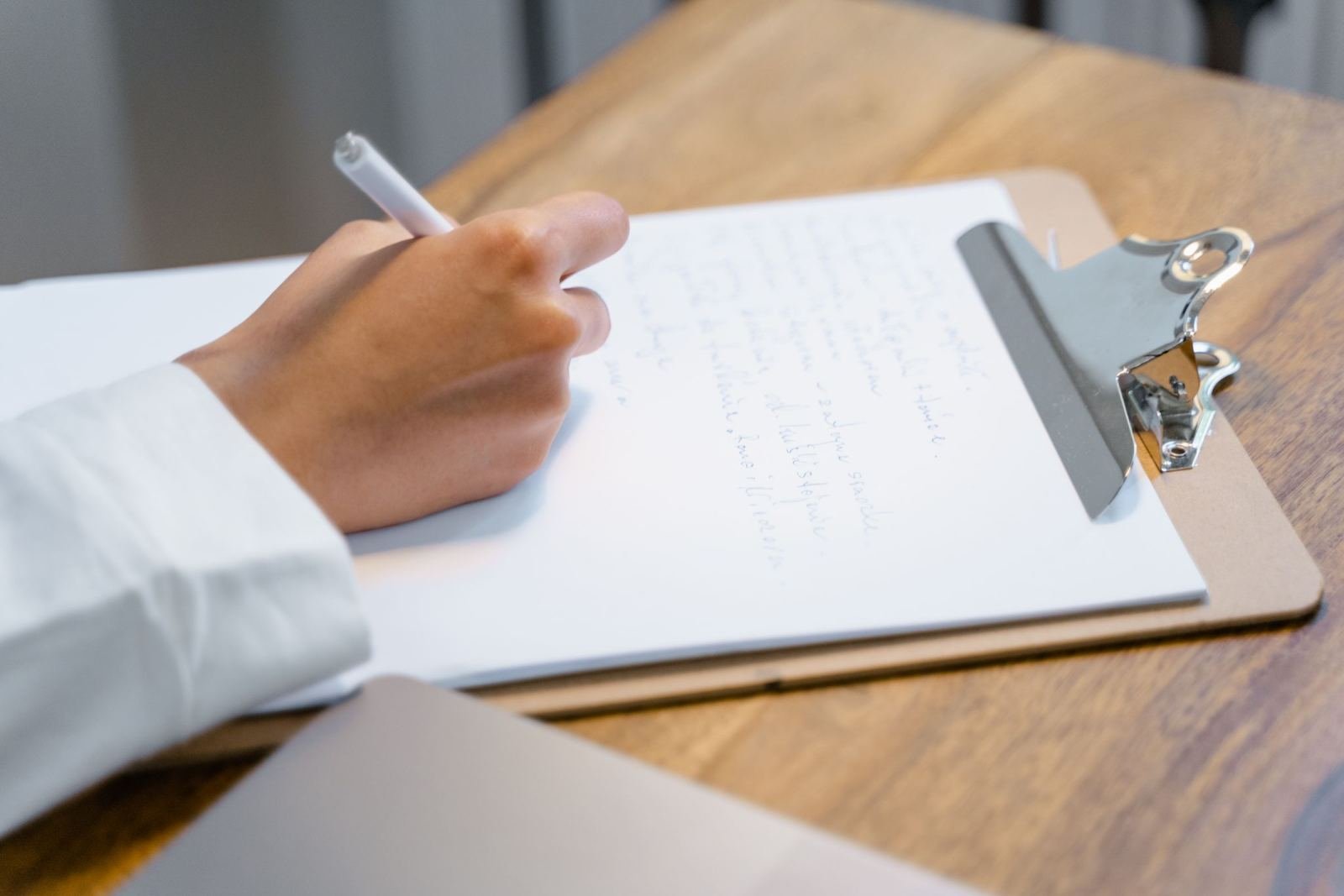A person writing on a clipboard resting on a wooden table