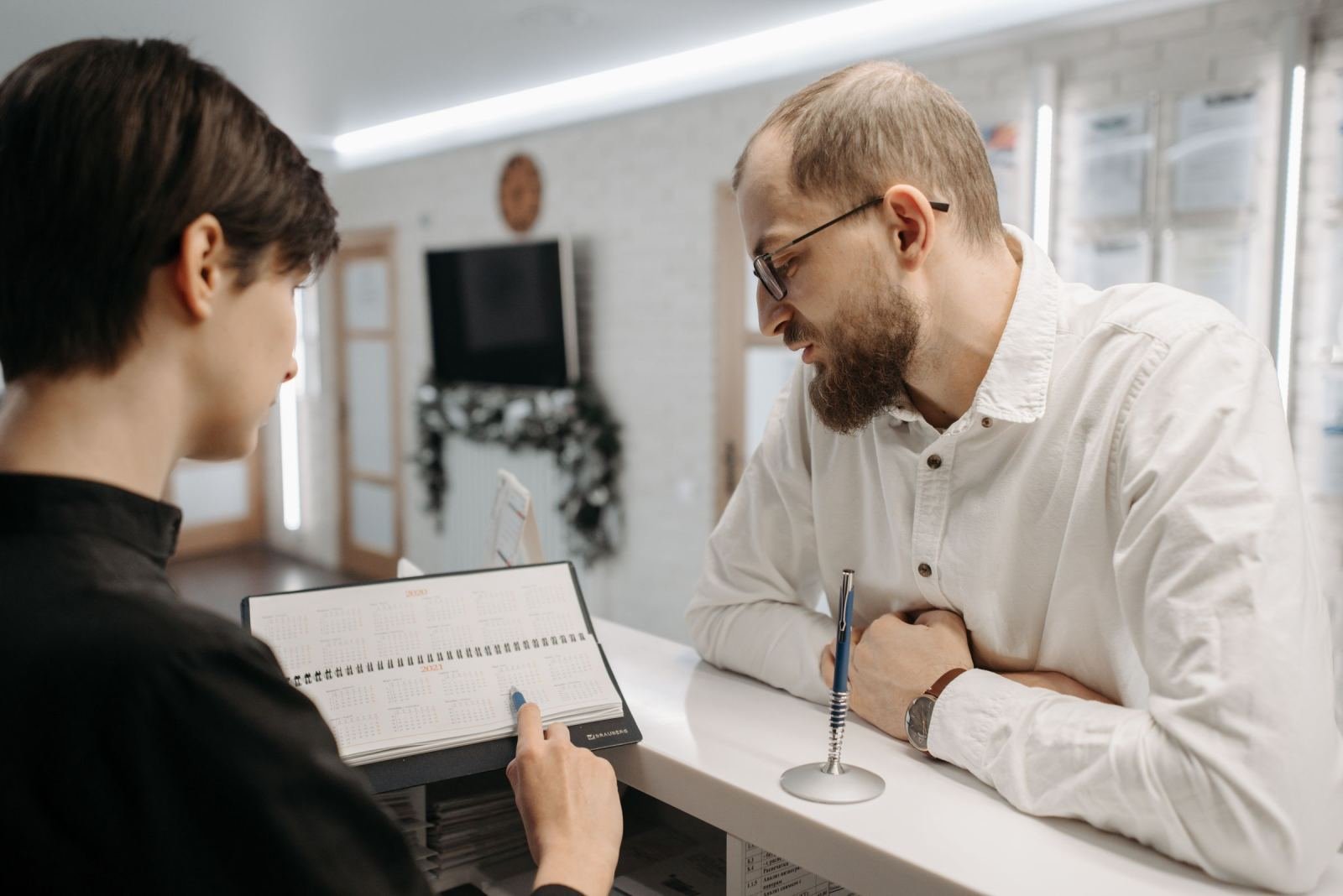 A man in a white shirt talks with a staff member at a white reception desk